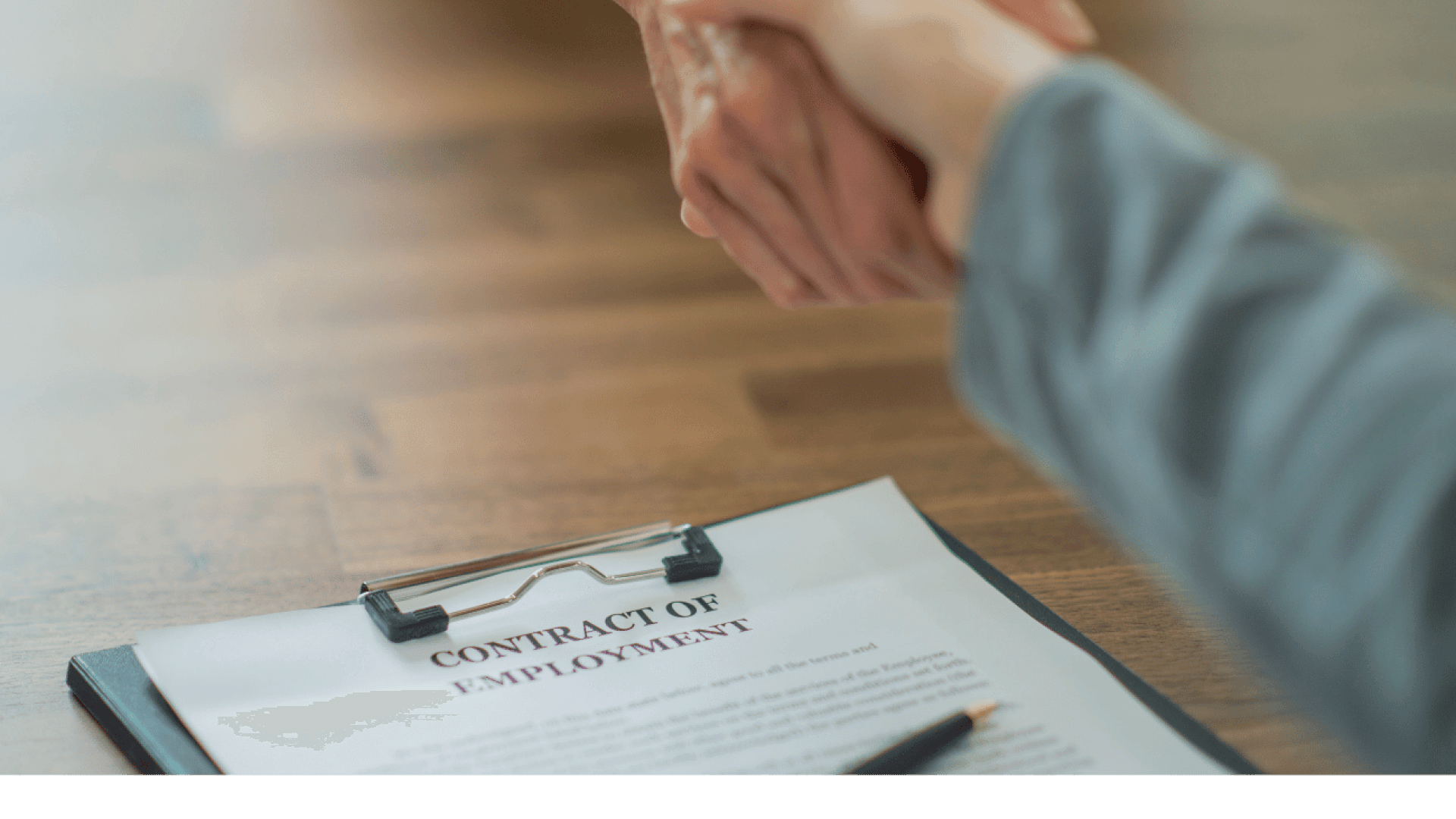 Two people shaking hands over a contract of employment