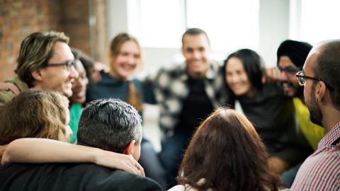 Large group of people standing in a circle with arms round shoulders